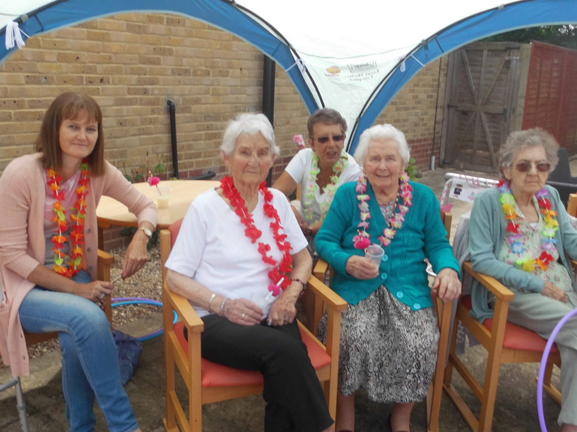 Woodstock Residential Care Home residents and family members in the garden wearing floral Hawaiian garlands