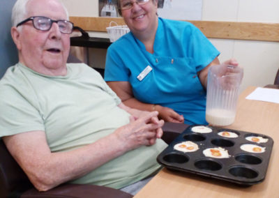 Hengist Field Care Home resident and staff member smiling to camera with his homemade mini-quiches in front of him
