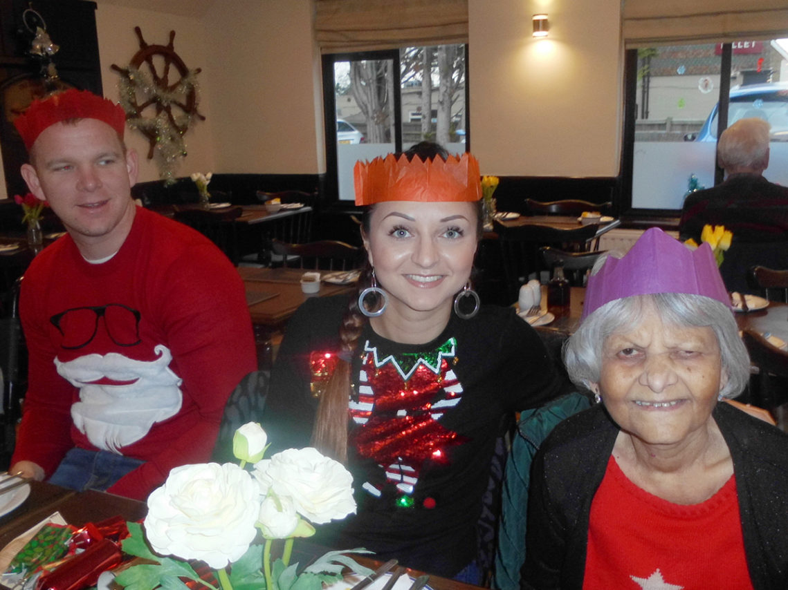 Residents, family and staff of Woodstock Residential Care Home enjoying fish and chips, wearing Christmas hats