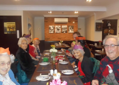Residents, friends and staff from Woodstock Residential Care Home around a table at Marino's restaurant, wearing Christmas hats