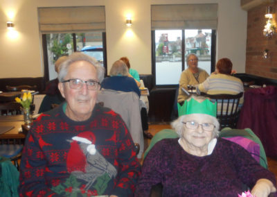 A lady and gentleman posing for a photo - wearing a Christmas jumper and Christmas party hat