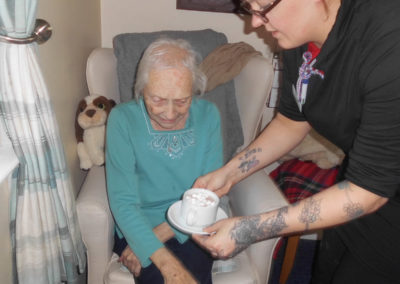 Lady resident at Woodstock Residential Care Home, sitting in a chair, being handed a hot chocolate