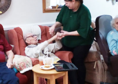 Meyer House Care Home resident holding the hand of a staff member while sitting in his chair