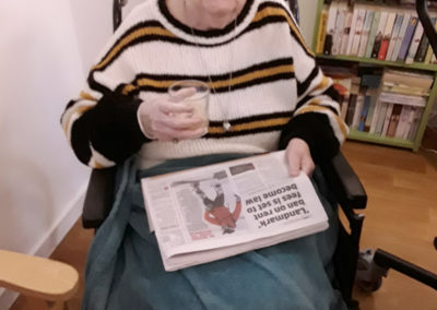 Lady resident sitting with a newspaper and a glass of Baileys