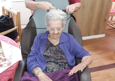 Lady resident sitting in a chair having her hair done by a hairdresser
