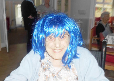 A woodstock lady resident smiling at the camera wearing a bright blue wig
