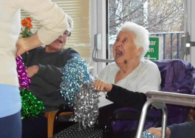 A lady from Woodstock Residential Care Home smiling with a sparkly pom pom, during an exercise class