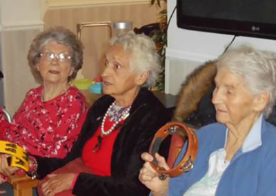 Three ladies from Woodstock Residential Care Home seated together with tambourines, during an exercise class