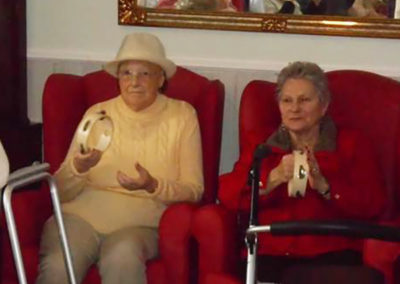 Two lady residents from Woodstock Residential Care Home sitting together during an exercise class, shaking tambourines