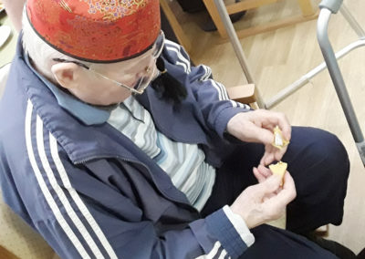 Gentleman resident sitting wearing a Chinese hat opening a fortune cookie