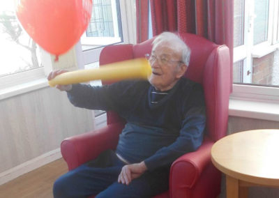 Male resident sitting in chairs with a soft tube, batting a red balloon