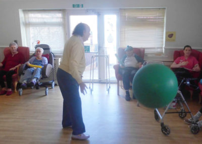 Residents in the lounge, playing with a large ball, during a seated exercise and music session