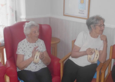 Two lady residents sitting next to each other playing tambourines