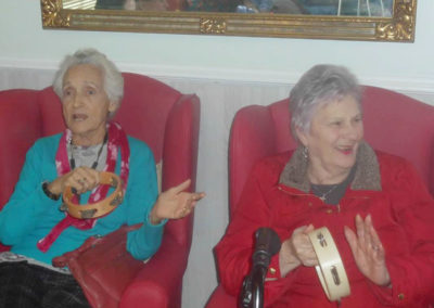 Two lady residents sitting together, smiling and playing tambourines