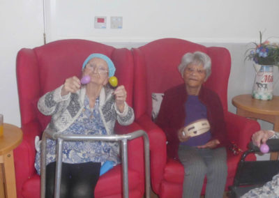 Two lady residents sitting together, smiling and playing musical instruments
