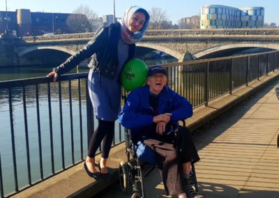 Resident in a wheelchair with a staff member, posing for a photo by the river