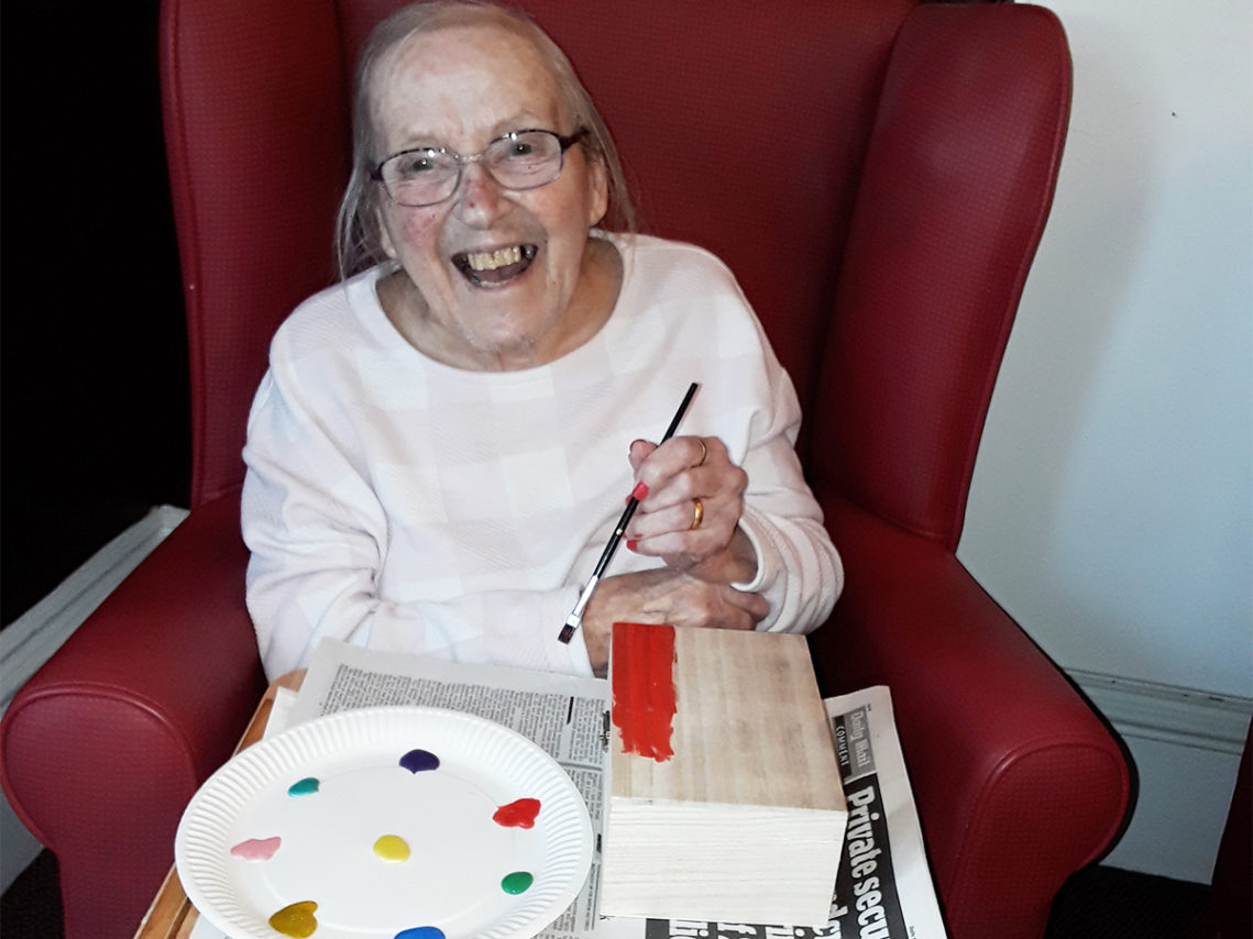 Resident painting a wooden treasure box with colourful paints at Lulworth House Residential Care Home