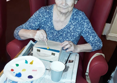 Resident painting a wooden box with colourful paints at Lulworth House Residential Care Home for Chinese New Year