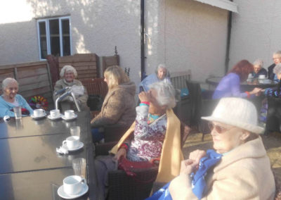 Residents and relatives sitting in the garden with tea and cake at Woodstock Care Home