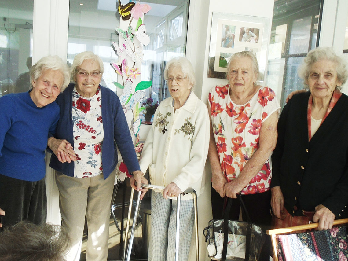 A group of lady residents standing together smiling at the camera at The Old Downs Residential Care Home