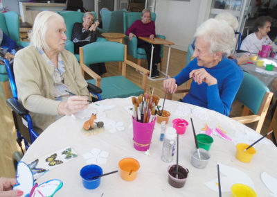 Lady residents sitting at a table, painting and colouring paper butterflies and leaves