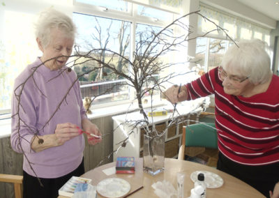 Two lady residents painting some tree twigs white to make into a Dignity Tree display