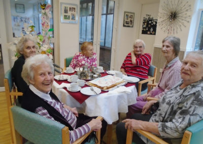Lady residents sitting at a table out to enjoy tea and a specially decorated Dignity Day cake