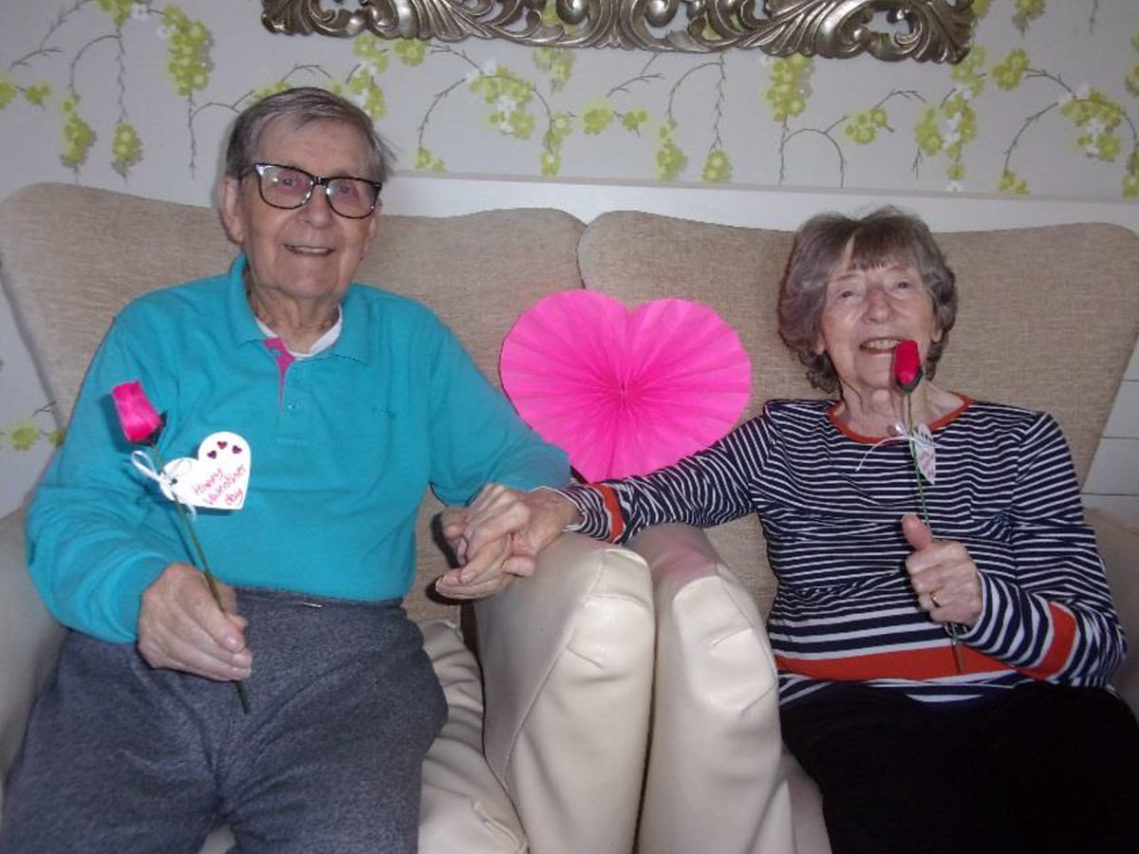 Residents smiling at the camera holding roses and a heart for valentines day