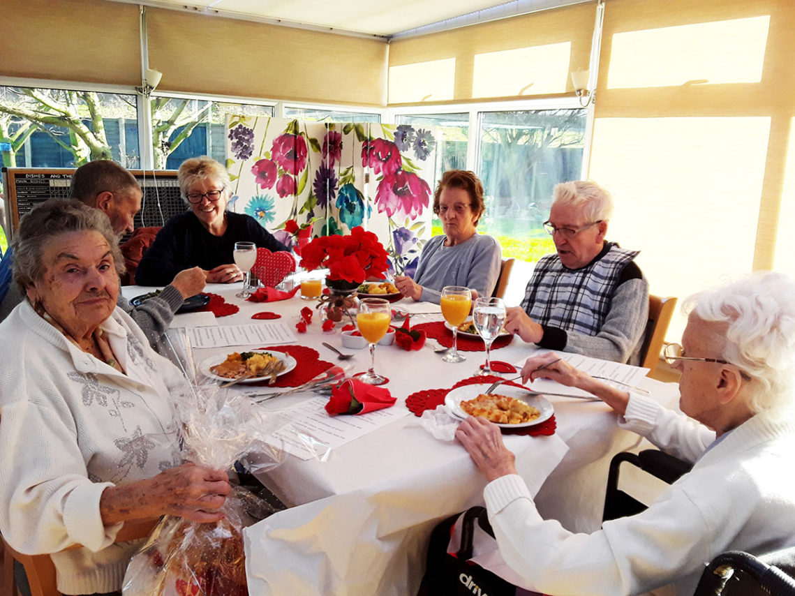 Residents and relatives around a decorated table enjoying a Valentines lunch together