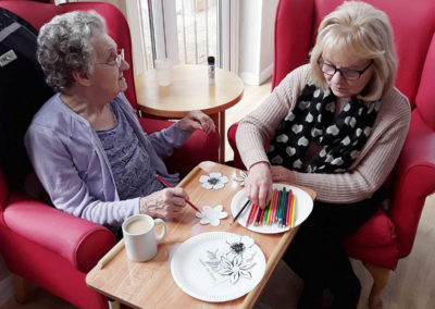Resident and visitor using coloured pencils to colour in a flower picture at Woodstock Residential Care Home