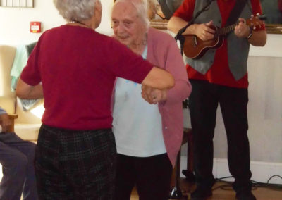 Two lady residents dancing together while Rob T plays music and sings