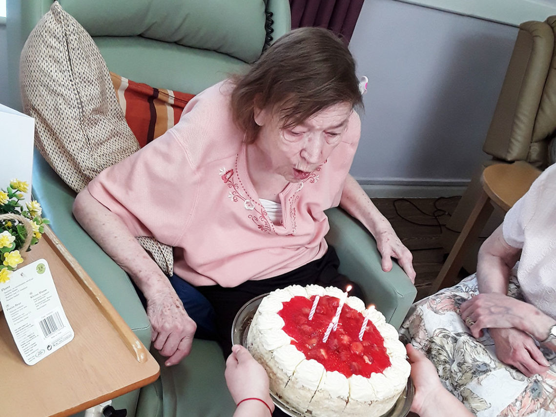 Resident Moira blowing out the candles on her strawberry birthday cake at Abbotsleigh Care Home
