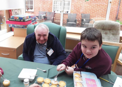Male resident at Princess Christian Care Home decorating cakes with a visiting child