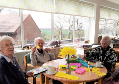 Lady residents sitting around a table making paper flowers for Mother's Day