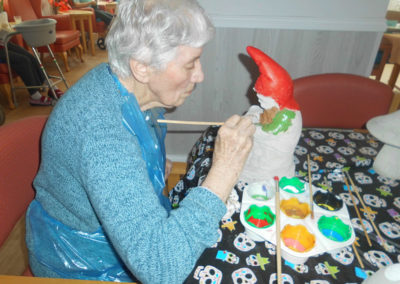 Lady sitting at a table painting the base of a pottery gnome