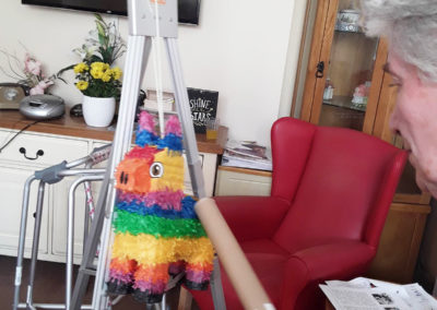 Lady resident hitting a multi coloured piñata