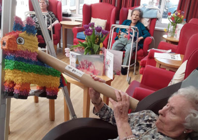 Lady resident hitting a colourful piñata in the lounge at Woodstock Residential Care Home