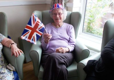 Lady resident in Sonya Lodge lounge waving a Union Jack flag and wearing a Union Jack hat