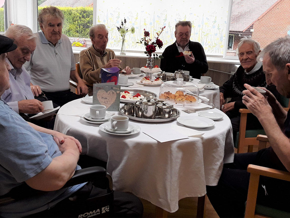 Male residents sitting around a table celebrating Fathers Day with a coffee morning at The Old Downs Residential Care Home
