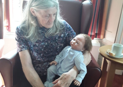 Lady resident at The Old Downs Residential Care Home sitting with a therapy doll on her lap