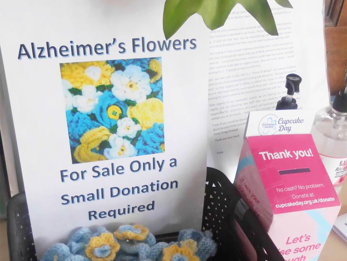 A poster and fundraising box for knitted forget-me-nots at Woodstock Residential Care Home