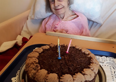 Female resident in bed, smiling with a chocolate birthday cake