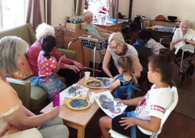 Residents and local nursery children painting pictures together around a table at Lulworth House