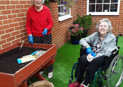 Two lady residents planting bulbs in a raised bed in the garden